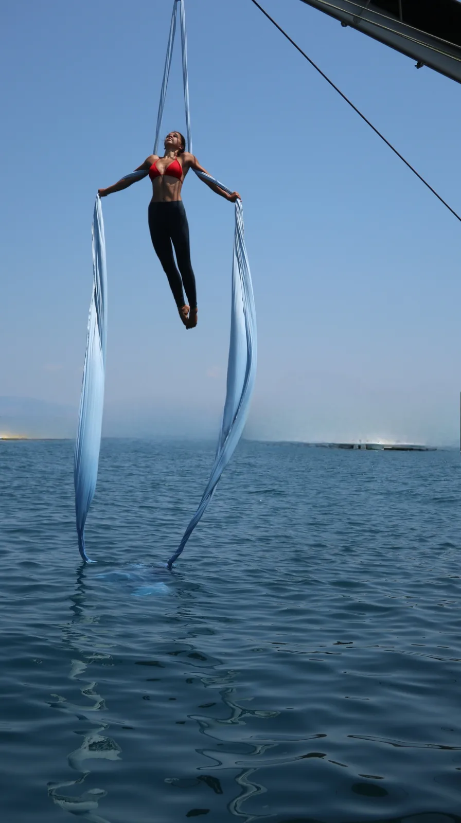 Distant figure suspended on pale silks over calm open water